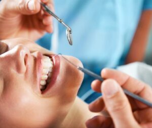 girl smiling with mirror and dental pick next to her mouth