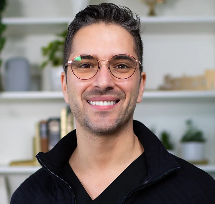 Headshot of Dr. Bakkali wearing a black jacket against a cabinet with some plants blurred background.